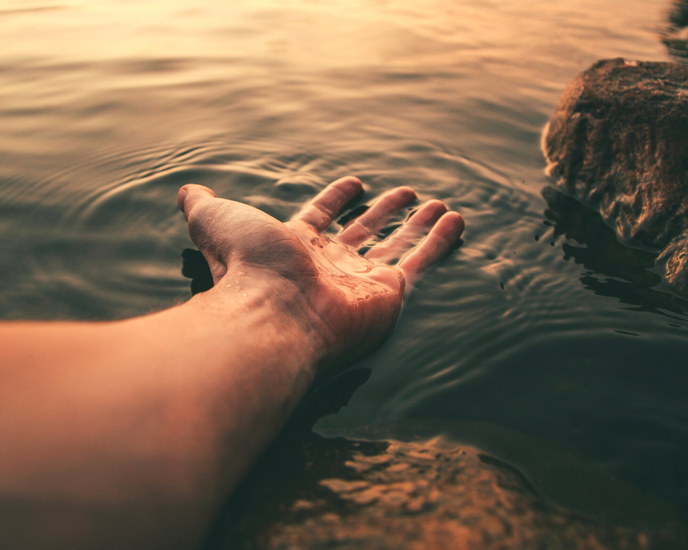 A hand inside the water along with a sun reflection